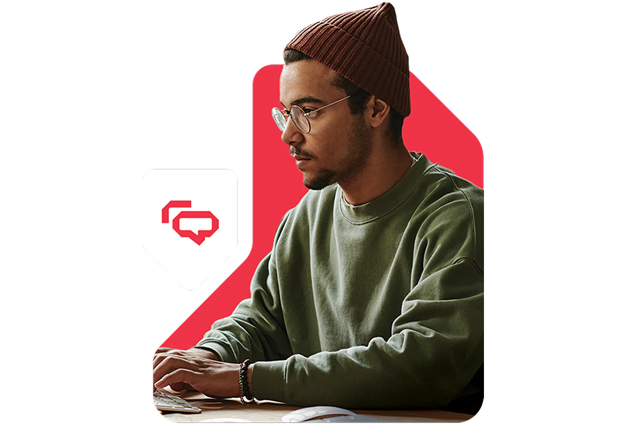 Man wearing glasses and a beanie typing on a laptop with chat icons in the background.